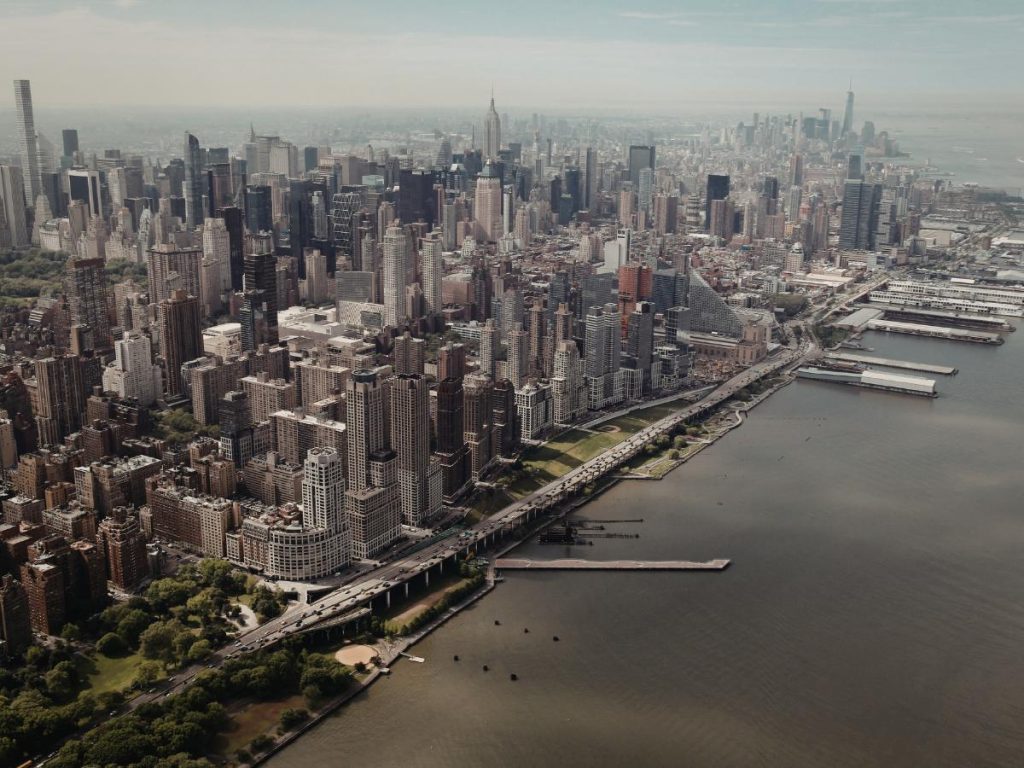 Vista aerea di un paesaggio urbano tentacolare con grattacieli densamente popolati che costeggiano il lungomare. La scena trasmette vivacità urbana e sviluppo industriale.
