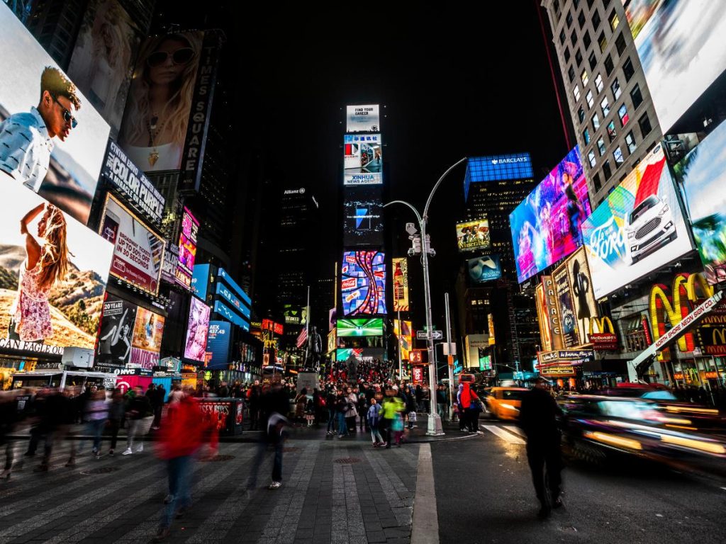 La vivace Times Square di notte, illuminata da vivaci cartelloni pubblicitari e luci al neon. Folle di persone e taxi creano un'atmosfera dinamica e vivace.