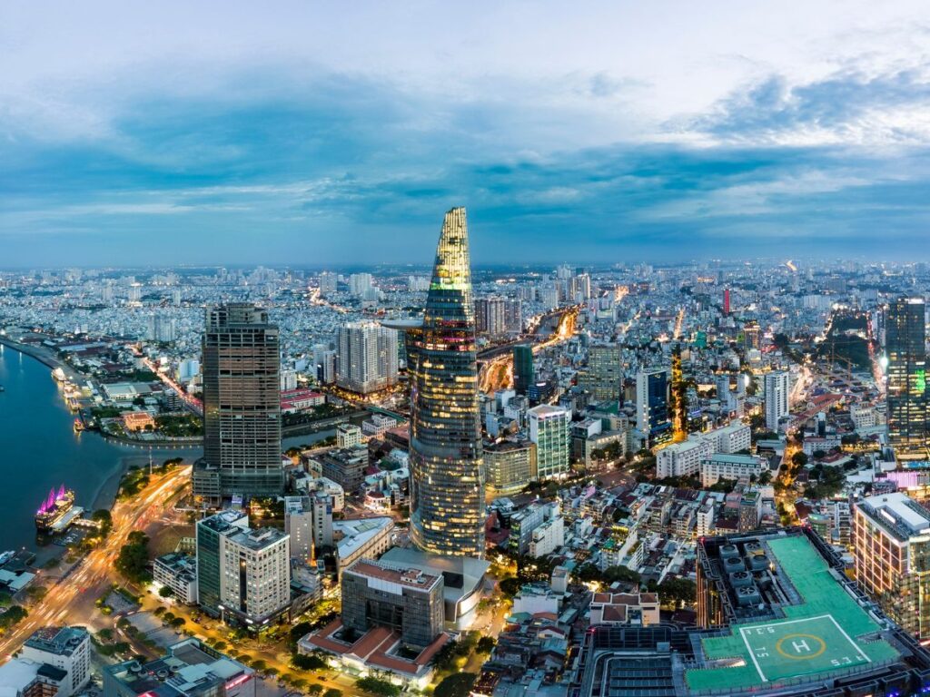 Vista aerea di Ho Chi Minh al tramonto, con grattacieli illuminati, un fiume tortuoso e strade trafficate che trasmettono energia urbana e crescita dinamica.