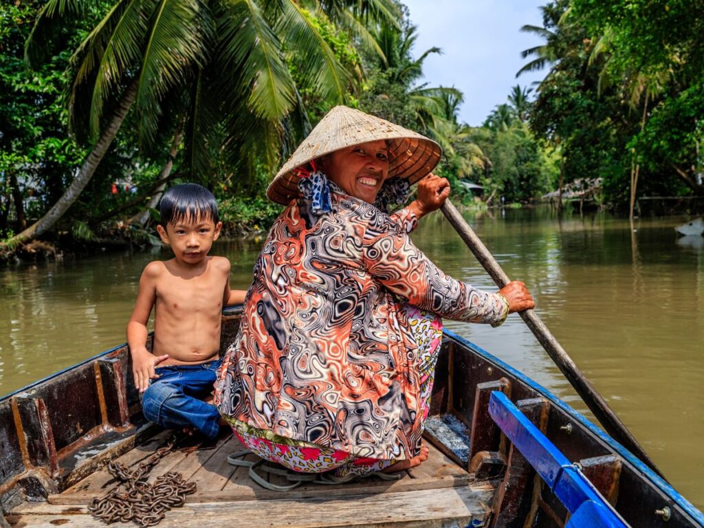 una donna vietnamita sta remando su una barchetta in legno sul delta del Mekong, con lei c'è un bimbo 