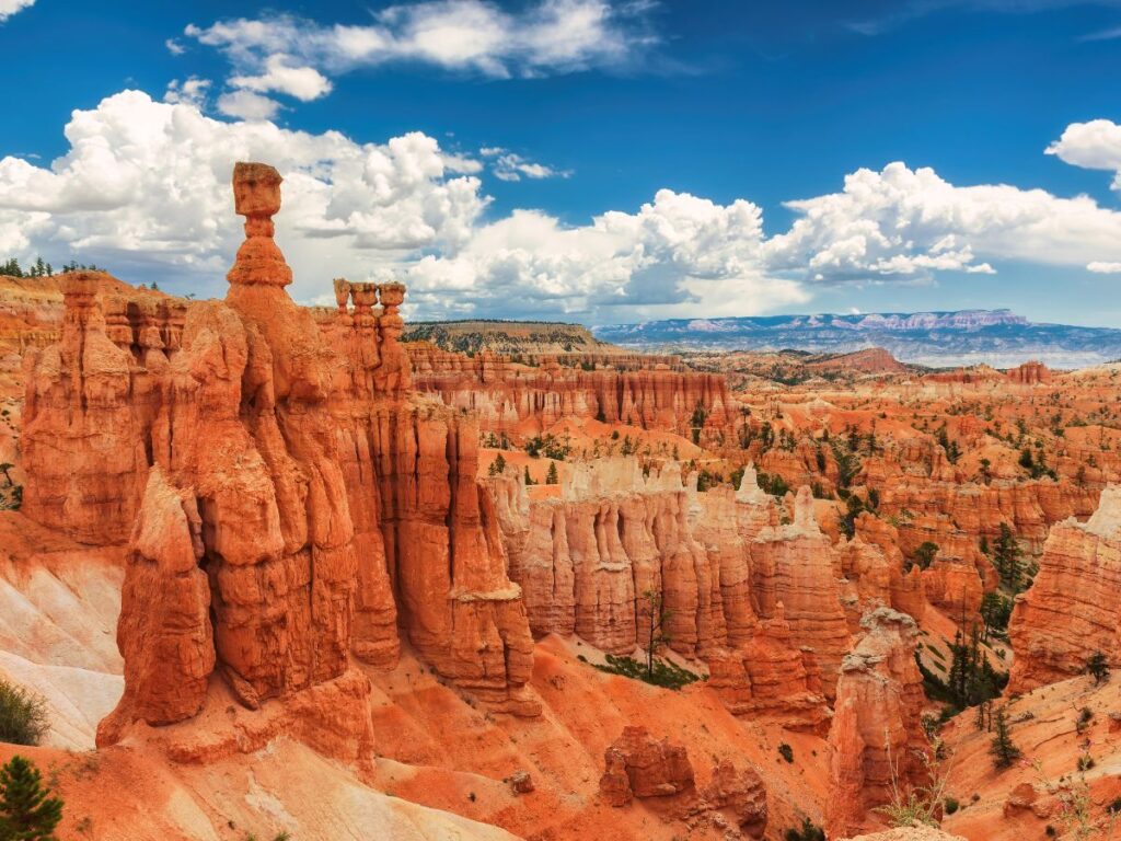 Vista maestosa dei pinnacoli rossi e arancioni del Bryce Canyon, tra  i parchi di Utah e Wyoming, sotto un cielo azzurro brillante con soffici nuvole. Il paesaggio è vasto e maestoso.