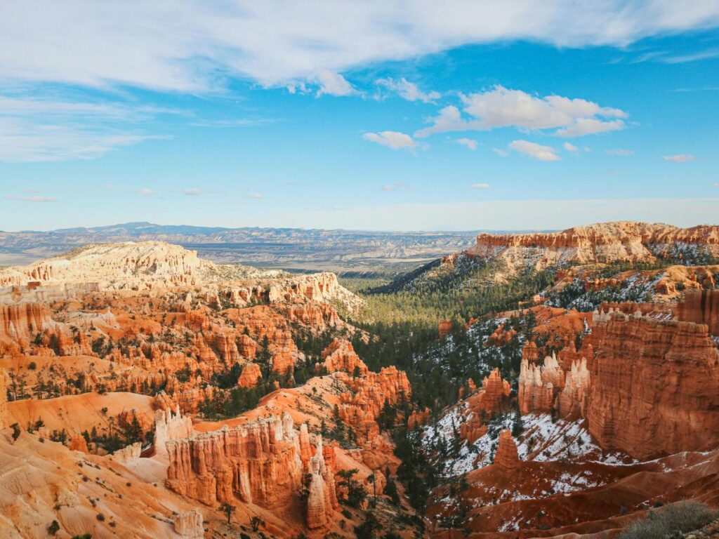 Vista panoramica del Bryce Canyon con suggestive formazioni rocciose rosse e hoodoo sotto un cielo azzurro brillante. Le macchie di foresta verde aggiungono contrasto.
