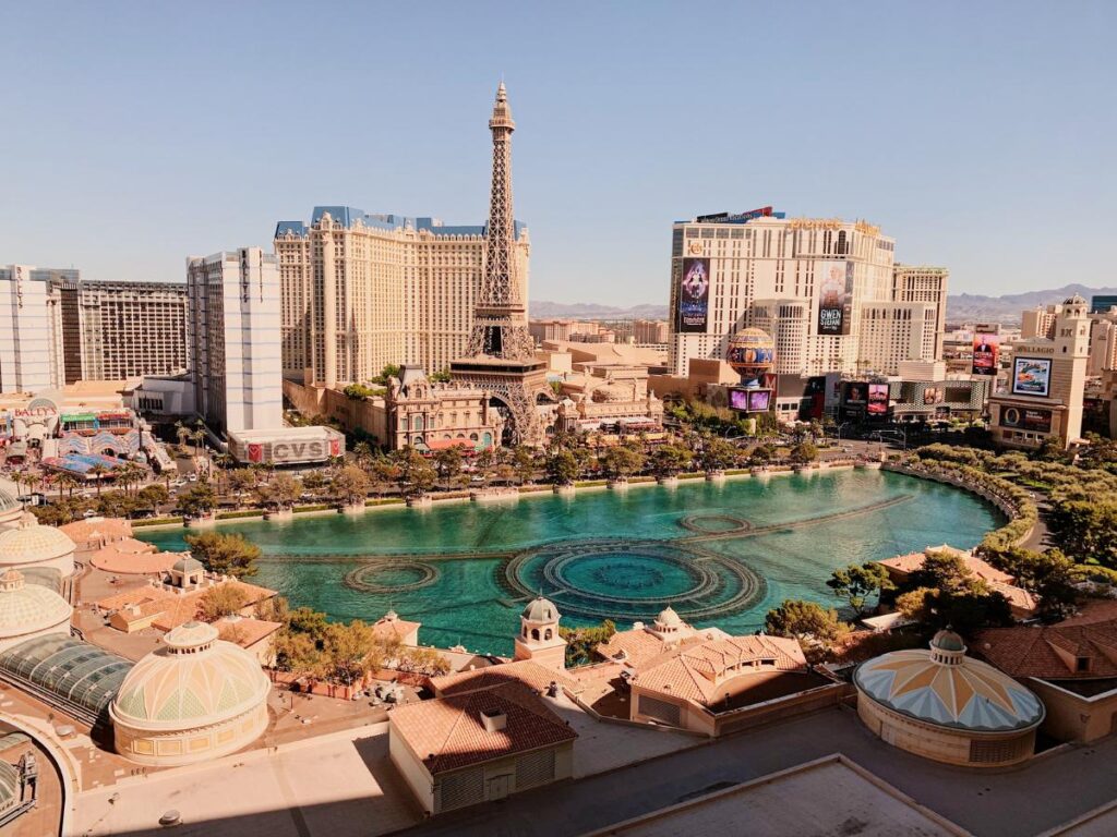 Vista aerea di Las Vegas con una fontana blu, una replica della Torre Eiffel e hotel sotto un cielo limpido, che trasmette un'atmosfera vivace e movimentata.
