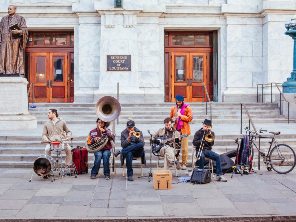 Una banda di strada si esibisce con strumenti quali tuba, tromba, banjo e batteria, all'esterno della Corte Suprema della Louisiana, creando un'atmosfera vivace.