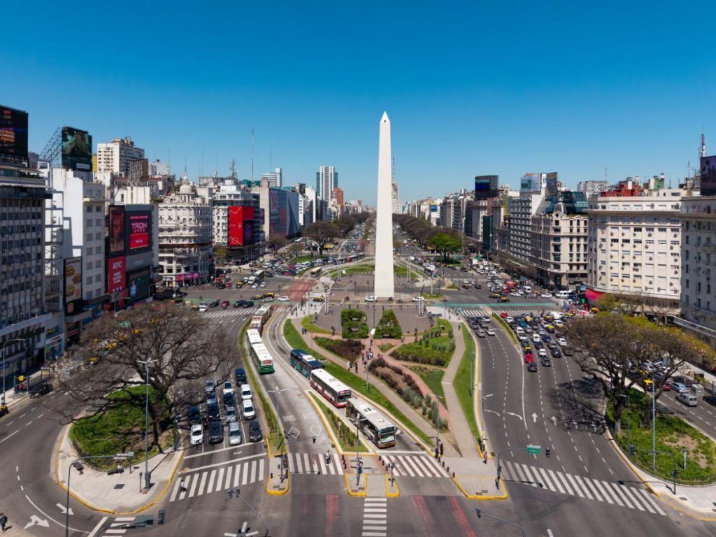 Veduta aerea della vasta Avenida 9 de Julio a Buenos Aires, con il grande obelisco bianco al centro e il traffico cittadino che scorre intorno alle aree verdi. Da vedere in 10 giorni in Argentina.