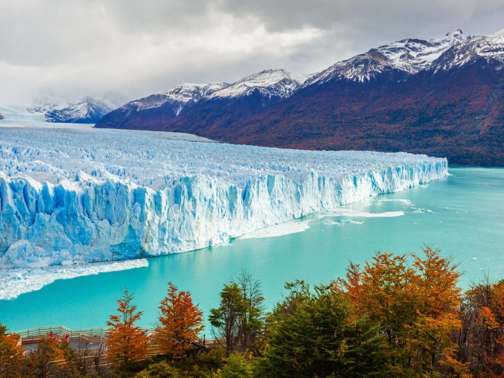 Una vista spettacolare del fronte del ghiacciaio Perito Moreno in Patagonia, con le sue pareti di ghiaccio azzurro che si tuffano nell'acqua turchese, incorniciato da alberi autunnali. Da vedere in 10 giorni in Argentina.