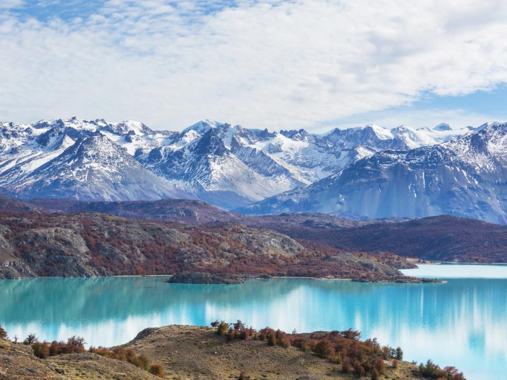Uno splendido paesaggio della Patagonia che mostra montagne innevate riflesse in un lago alpino dalle acque turchesi e cristalline.