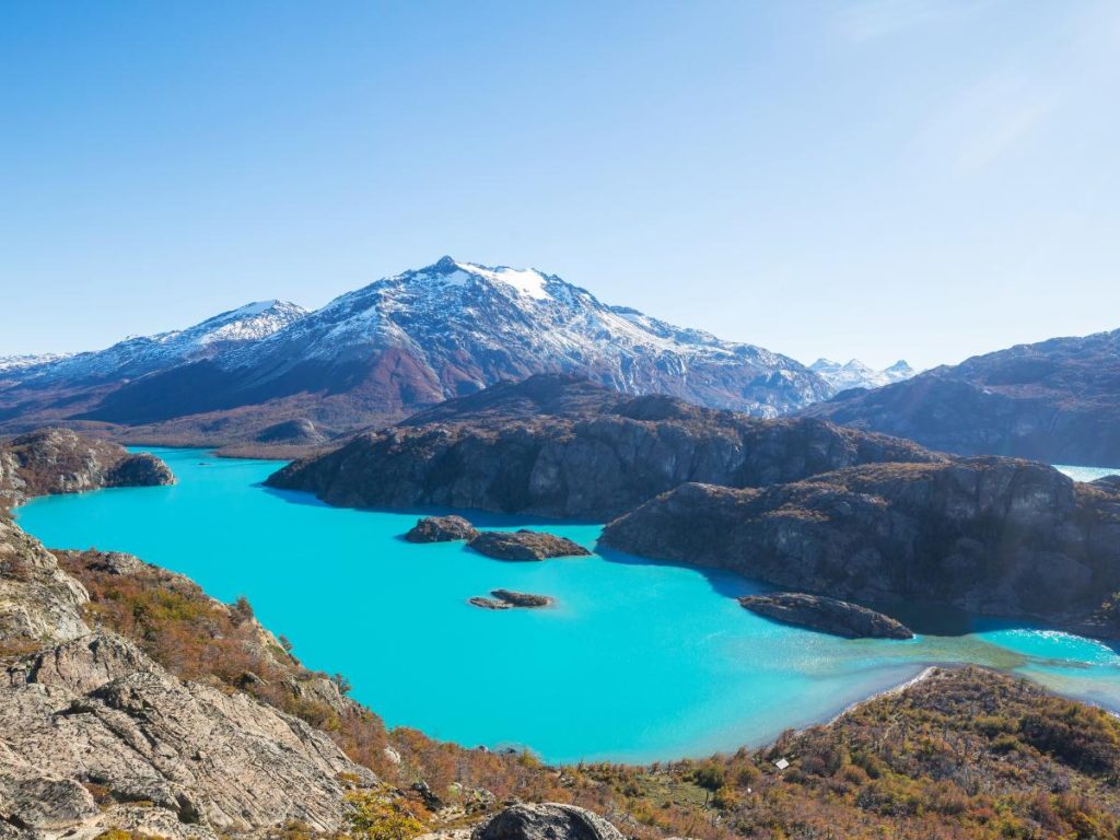 Una vasta inquadratura dall'alto di un lago color turchese intenso punteggiato da piccole isole, circondato da aspre montagne e vegetazione selvatica.