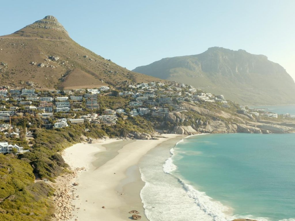 Una veduta panoramica di Clifton Beach a Città del Capo, tra le destinazioni perfette dove andare in estate, con sabbia bianca, mare turchese, case di lusso sul pendio della collina e la sagoma della montagna Lion's Head sullo sfondo