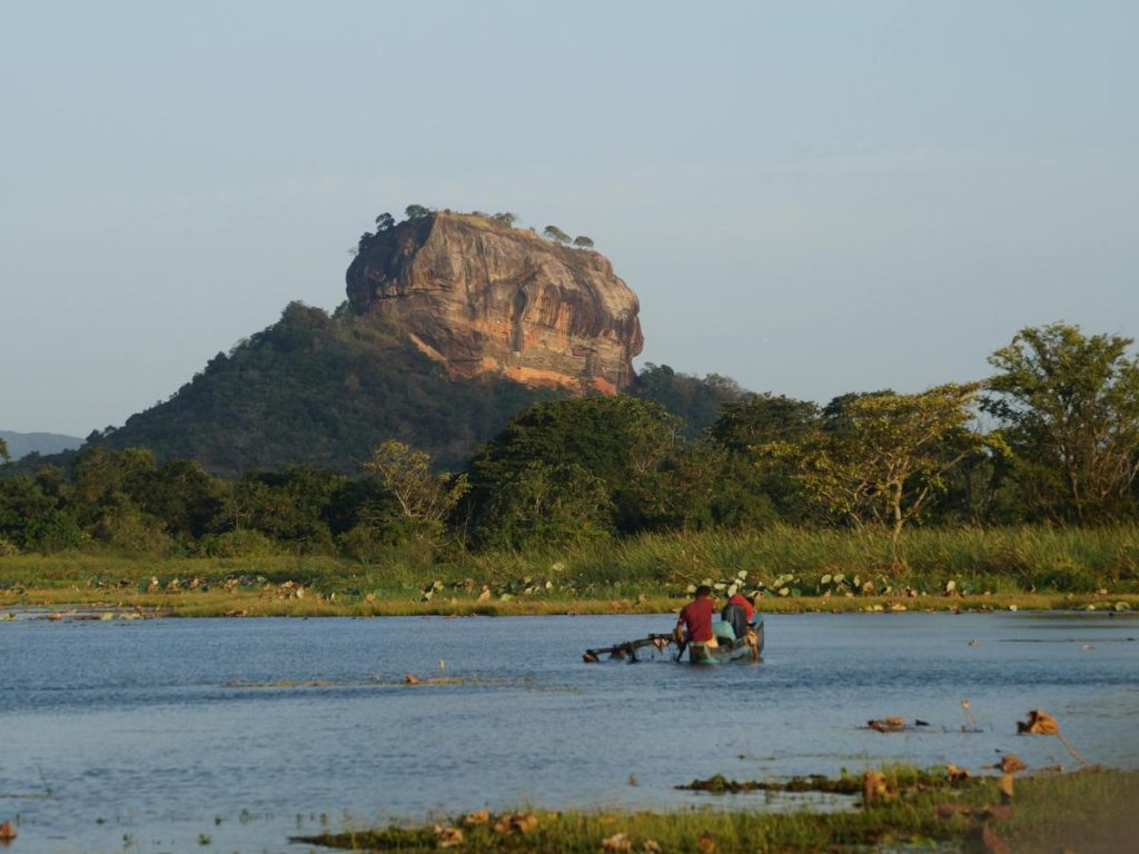 La maestosa fortezza rocciosa di Sigiriya in Sri Lanka che svetta sopra la giungla, vista da un lago in primo piano dove si scorge una piccola imbarcazione di pescatori, tra le destinazioni perfette da visitare in estate