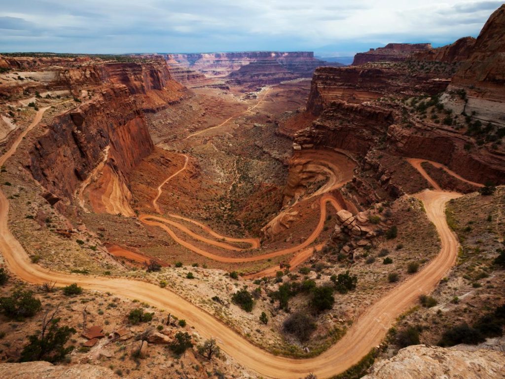 Una spettacolare veduta dall'alto dello Shafer Trail nel Canyonlands National Park. La strada sterrata forma stretti e vertiginosi tornanti che scendono lungo i fianchi di un profondo canyon dalle pareti rocciose stratificate nei toni del rosso e dell'arancio.