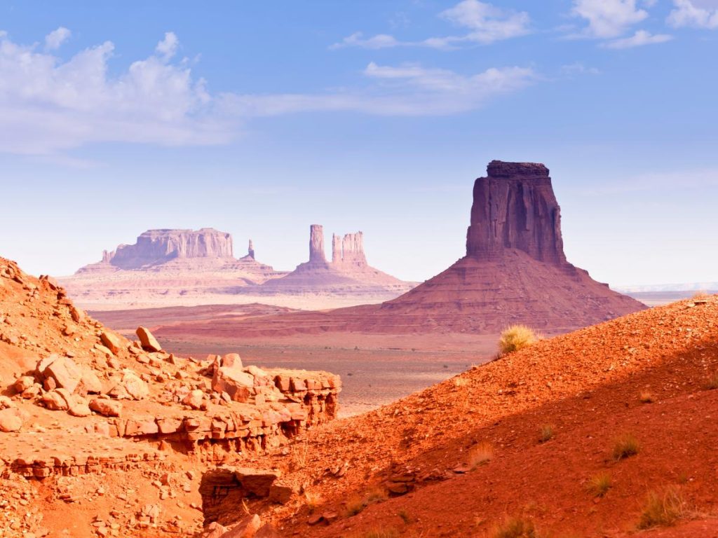 I celebri monoliti di roccia rossa della Monument Valley che si stagliano nel deserto americano sotto un cielo sereno, tipico panorama da viaggio on the road nel West, da vedere durante un viaggio in nord America con scalo a Dublino.
