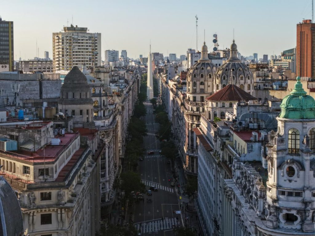Veduta aerea prospettica di un viale nel centro di Buenos Aires fiancheggiato da palazzi storici, con l'Obelisco che si staglia sullo sfondo. Da vedere durante un viaggio in Argentina.
