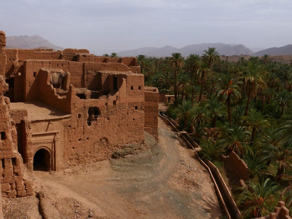 Antichi edifici in terra e paglia di una kasbah ad Agdz affacciati su una fitta oasi di palme da dattero e montagne sul fondo.