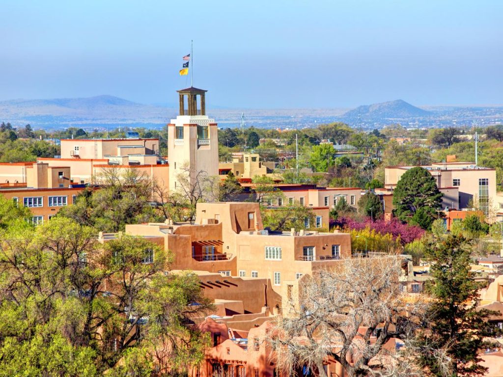 Veduta panoramica di Santa Fe in New Mexico, caratterizzata da edifici nel tipico stile architettonico Pueblo in mattoni di adobe color terra, circondati da alberi e montagne sullo sfondo.