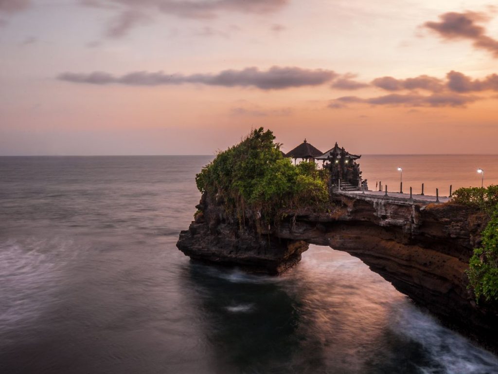 Tempio di Batu Bolong a Bali situato su un ponte di roccia naturale sul mare al tramonto, da vedere durante un viaggio originale in Indonesia.