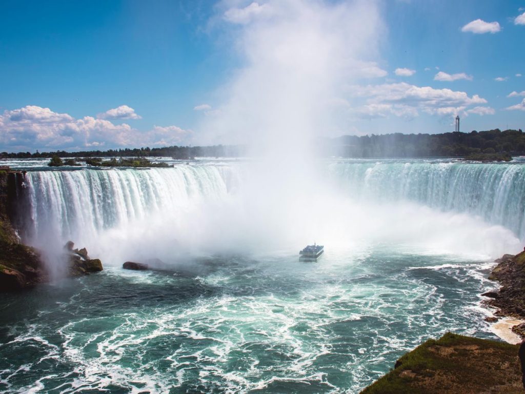 Cascate del Niagara imponenti con una battello turistico nelle acque agitate ai piedi della cascata Horseshoe, sotto un cielo azzurro e una fitta nube di vapore. Da vedere durante un viaggio di 15 giorni in Canada.