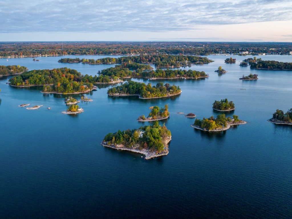 Vista aerea panoramica della regione delle Thousand Islands, con numerose piccole isole verdeggianti punteggiate di alberi autunnali sparse nell'acqua blu.
