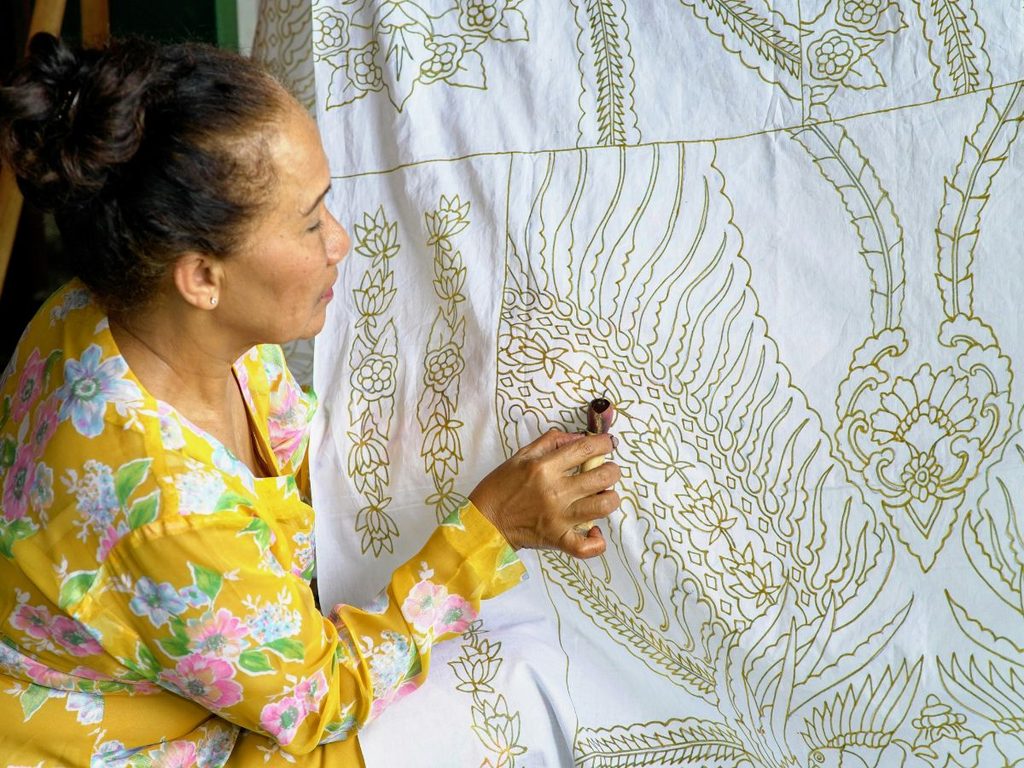 Artigiana giavanese che decori a mano un tessuto bianco con la tecnica tradizionale del batik.