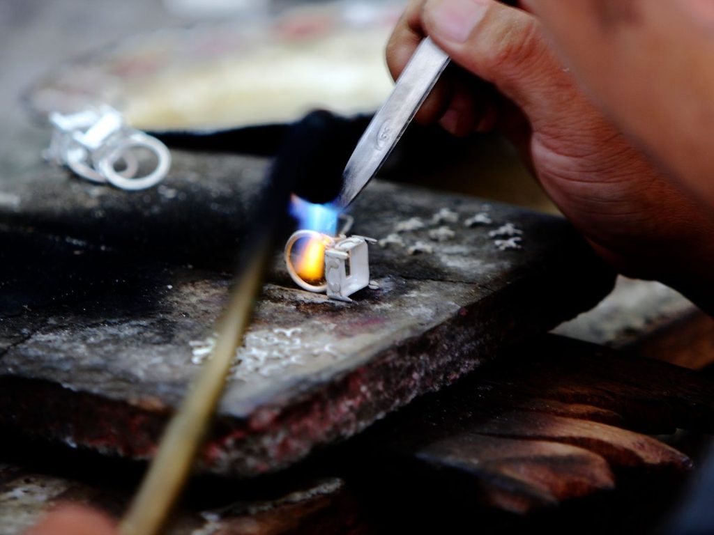Artigiano a Celuk lavora un anello d’argento con la fiamma sul banco di lavoro di un laboratorio di gioielleria.