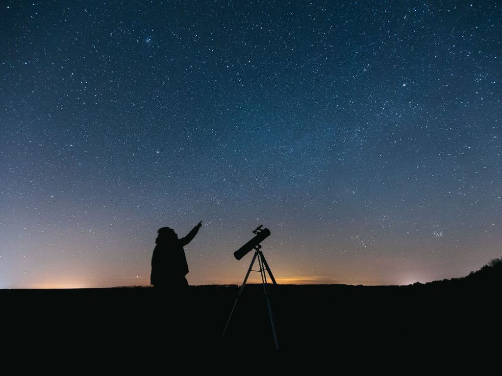 Sagoma di una persona accanto a un telescopio che indica il cielo stellato, durante una sessione di stargazing, esperienza per vivere una Bali autentica.