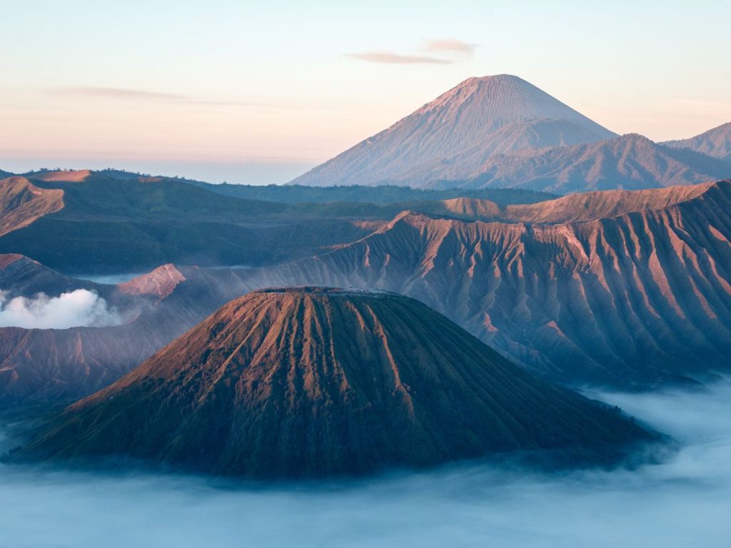 Il cono del Monte Batok tra le nebbie della caldera del Tengger, con un grande vulcano sullo sfondo